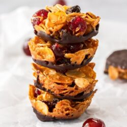 A stack of 4 florentines biscuits wiht a glace cherry in front, on a sheet of baking paper