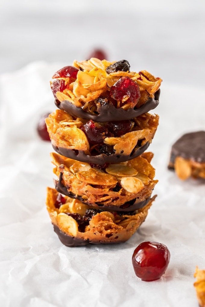 A stack of 4 florentines biscuits wiht a glace cherry in front, on a sheet of baking paper
