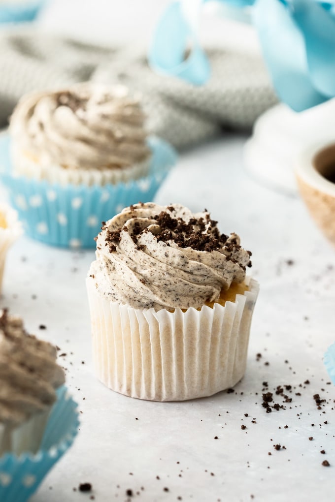 A cupcake in a white wrapper with oreo buttercream and topped with oreo crumbs.
