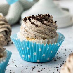 Closeup of a cupcake in a blue polka dot wrapper, topped with oreo buttercream