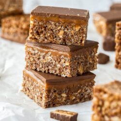 A stack of 3 snickers rice krispie treats on a sheet of white baking paper