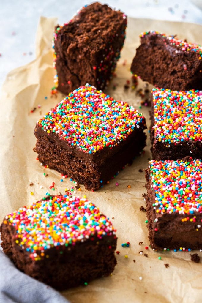 6 square slices of chocolate cake topped with sprinkles on a piece of brown parchment paper