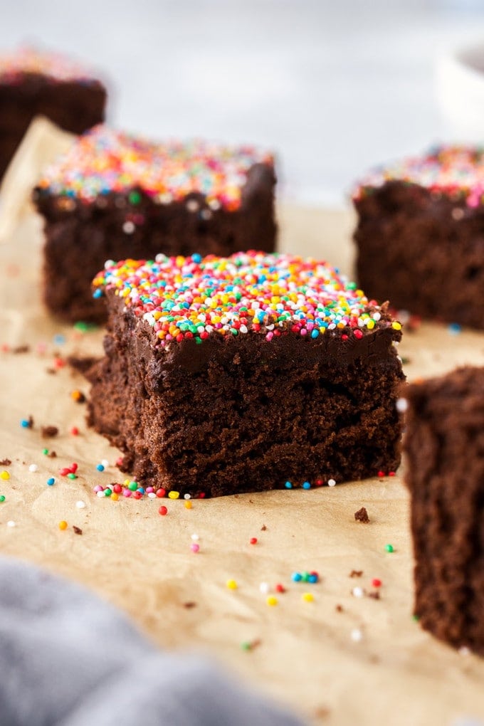closeup of a piece of chocolate cake topped with sprinkles on a piece of brown parchment paper