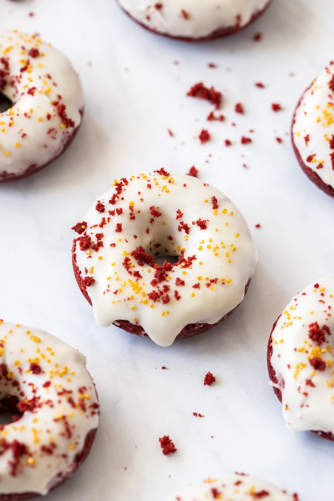 A birdseye view of a donut with white icing and red velvet crumbs, surrounded by more donuts