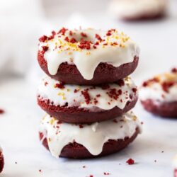 A stack of 3 red velvet donuts with white icing