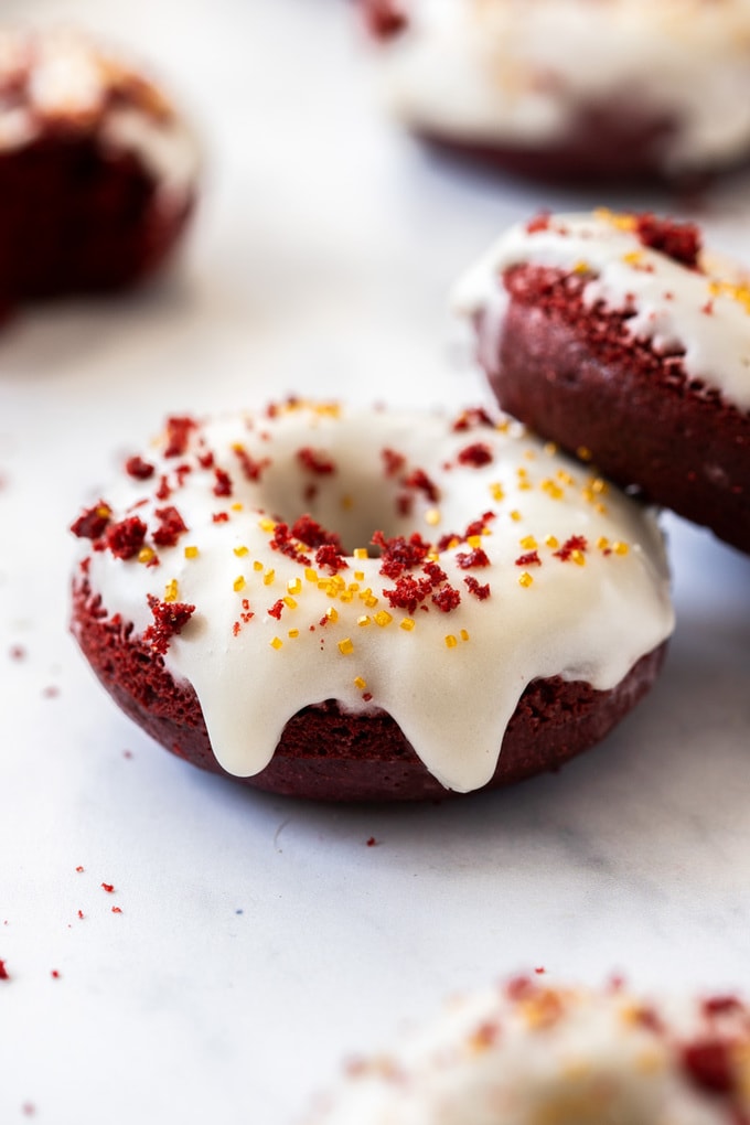 A closeup of a red velvet donut with white icing with another leaning on top of it