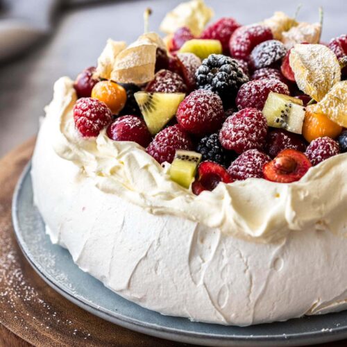 Close up of a pavlova toppedw with whipped cream and fruit on a wooden platter