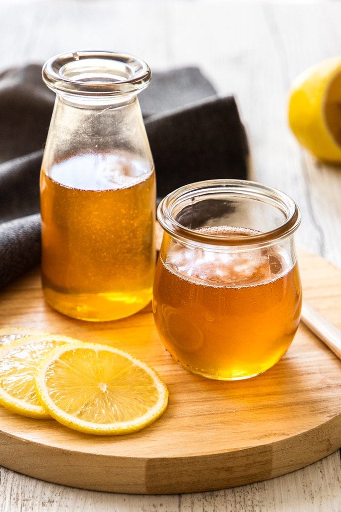 A jar and bottle both filled with lemon syrup, sitting on a wooden board.