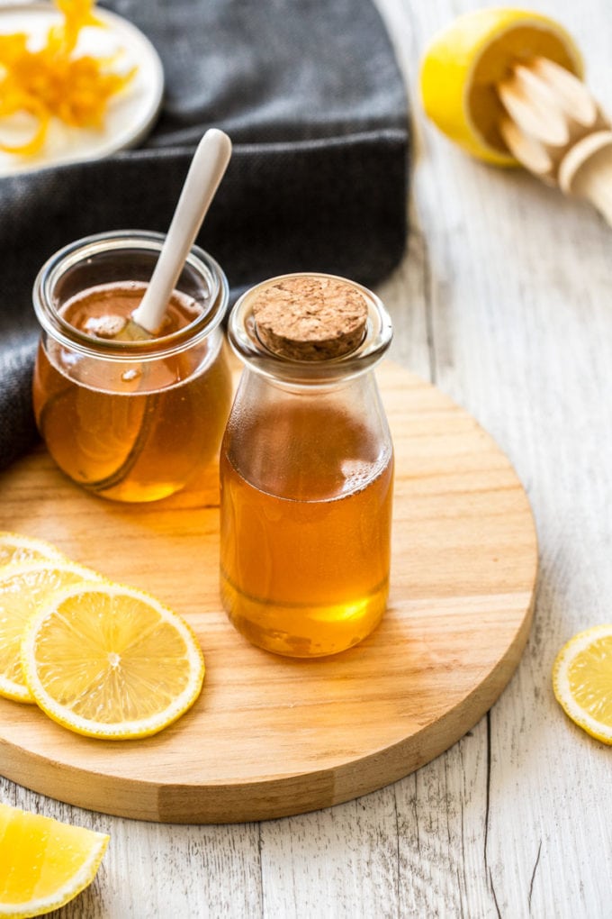 A jar and bottle both filled with lemon syrup, sitting on a wooden board.