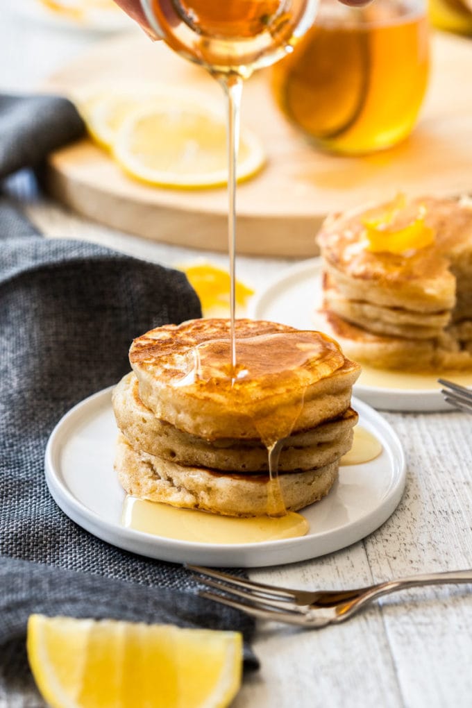 Lemon syrup being poured over a stack of pancakes.