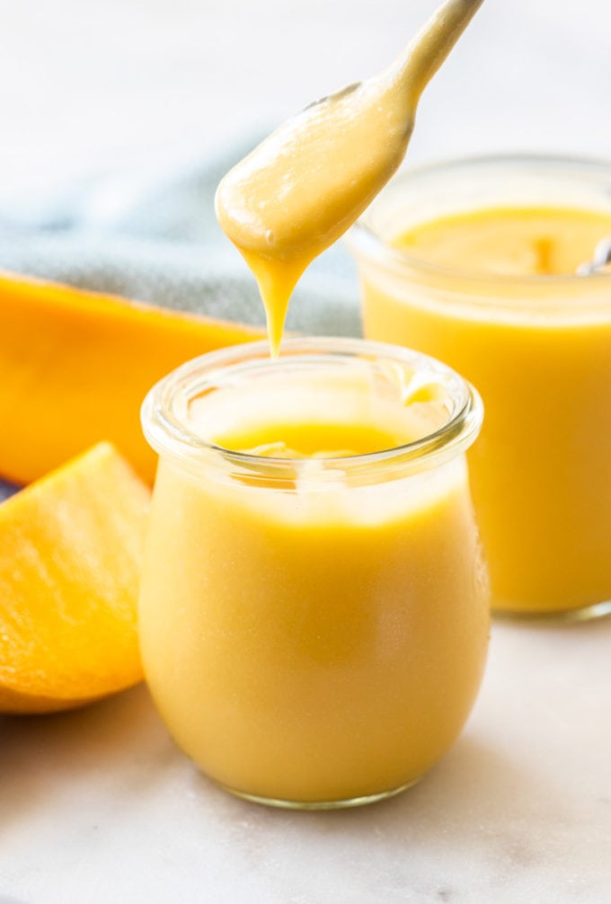 A spoon lifting out of a jar of mango curd.