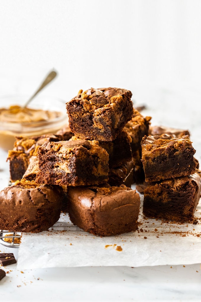A pile of brownies with a bowl of biscoff spread in the background.