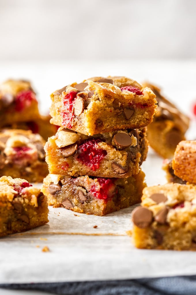 A stack of blondies with chocolate chips and raspberries on a sheet of baking paper with a grey tea towel underneath