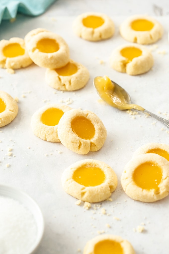 A batch of lemon curd cookies on a sheet of baking paper with a spoon of lemon curd next to them