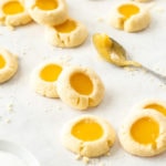 A batch of lemon curd cookies on a sheet of baking paper with a spoon of lemon curd next to them