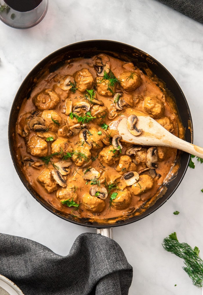 A black pan filled with meatball stroganoff with a wooden spoon in it