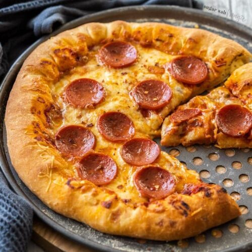 A pepperoni pizza on a metal tray on a wooden background. Once slice is cut out