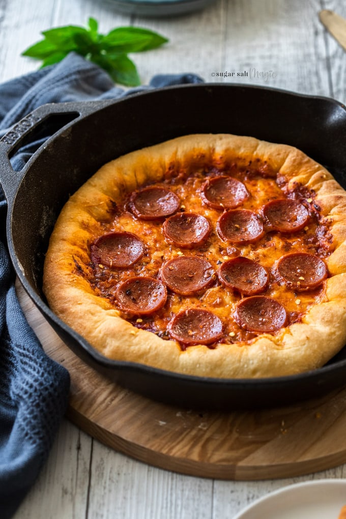 A stuffed crust pepperoni pizza in a cast iron skillet on a white wooden background