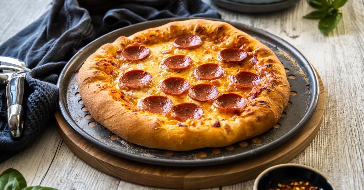 A stuffed crust pepperoni pizza on a metal tray on a wooden background