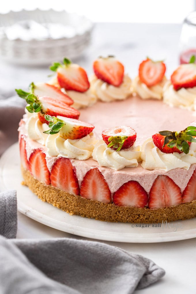 A pink cheesecake topped with strawberries on a marble background