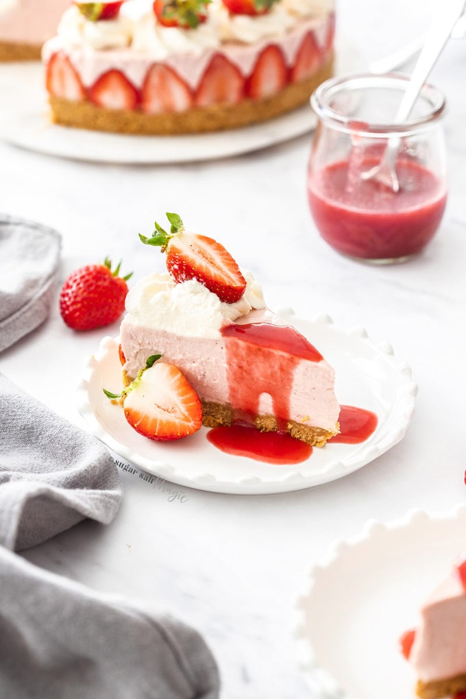 A slice of strawberry cheesecake with strawberry sauce, whipped cream and fresh berries, on a white plate