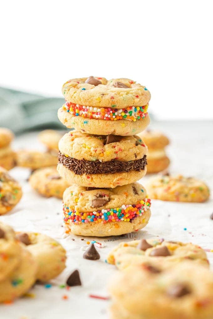 A stack of sandwiched funfetti cookies surrounded by more cookies, chocolate chips, and sprinkles.
