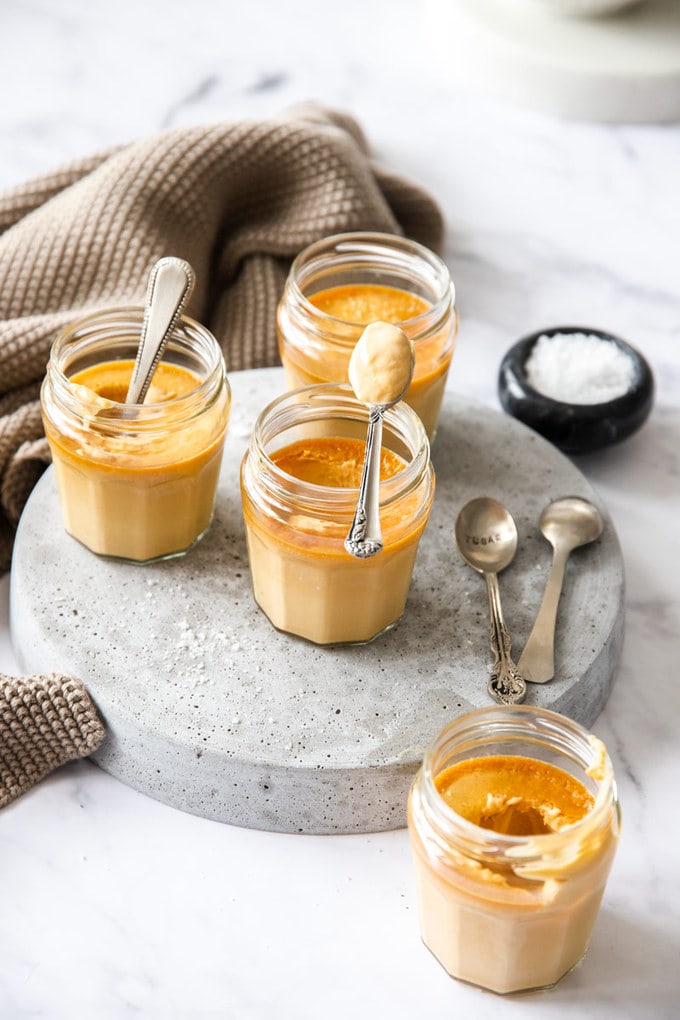 Small glass jars on a grey platter, filled with caramel custard