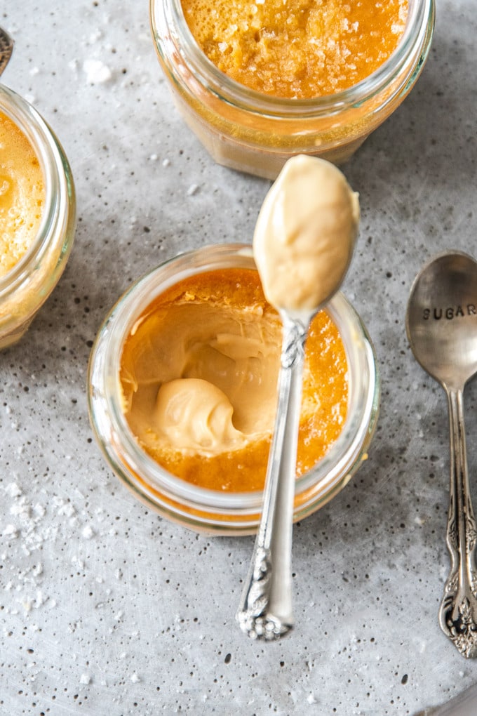 A small glass jar filled with caramel custard with a spoon sitting on top