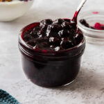 A small glass jar, filled to the brim with blueberry pie filling.