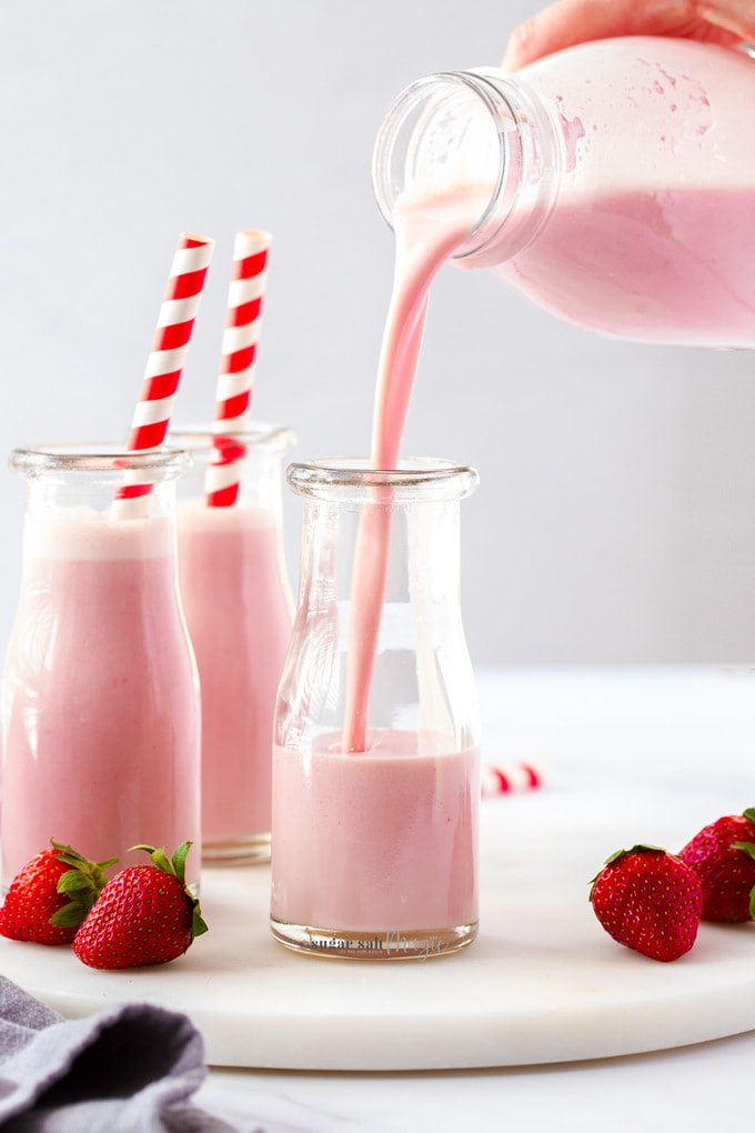 Two bottles of strawberry milk, with more being poured into a third bottle