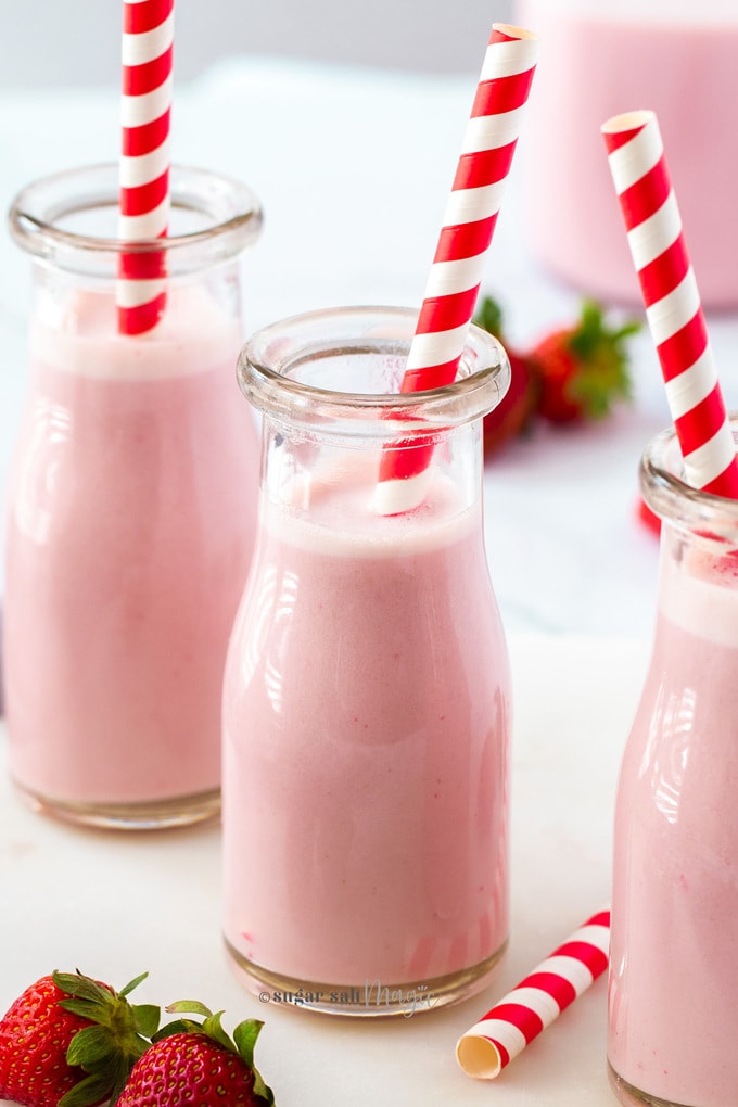 Strawberry milk in small glass bottles with stripe red straws on a marble platter