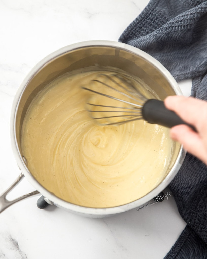 Thick pastry cream in a saucepan with a whisk in it.