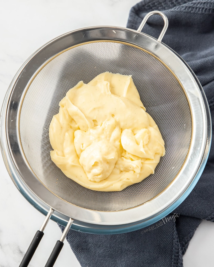Vanilla pastry cream in a strainer over a glass bowl