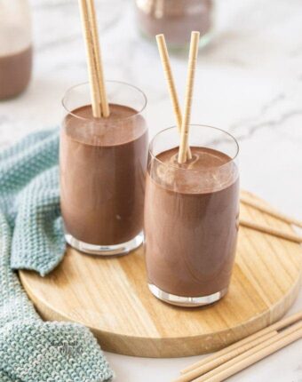 2 glasses of chocolate milk sitting on a small wooden platter