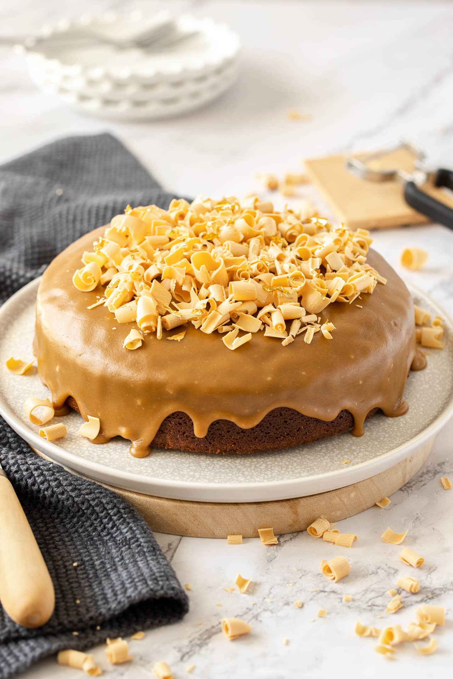 A caramel coloured cake topped with white chocolate on a white plate