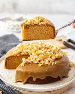A slice of caramel cake being held above the remaining cake