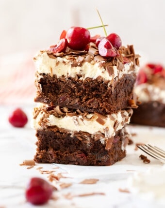 Two brownies stacked, topped with cream, cherries and chocolate