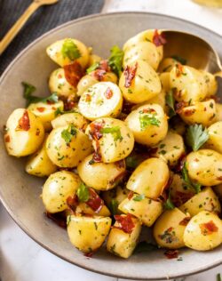 Closeup of a bowl full of cooked potatoes with pieces of prosciutto and parsley
