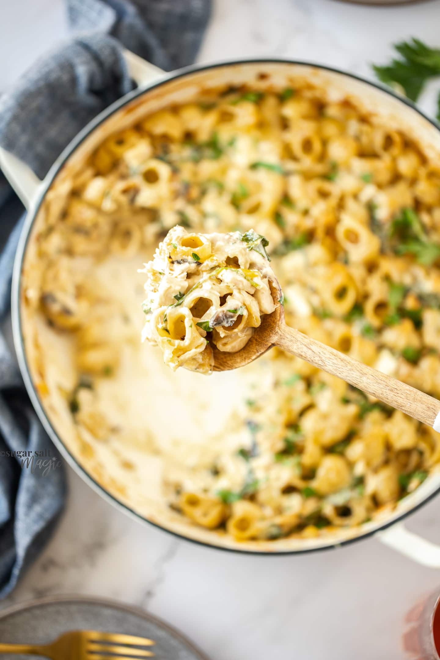 A spoon filled with pasta hovering over a white pan full of pata