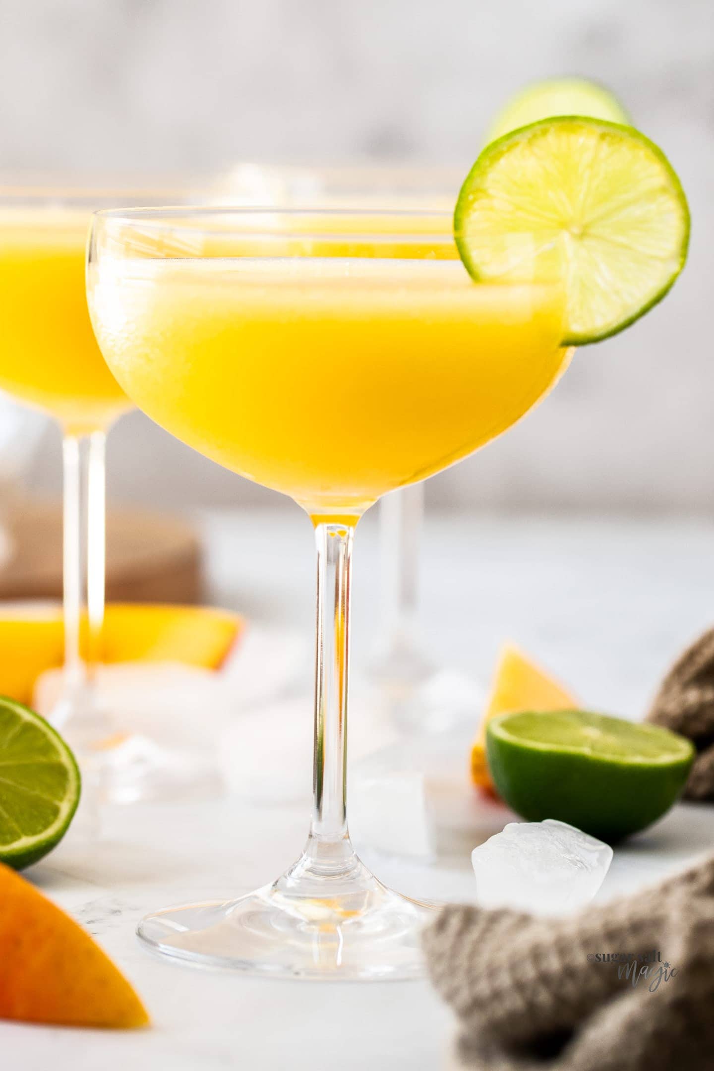 A champagne saucer filled with mango daiquiri with a slice of lime on the edge