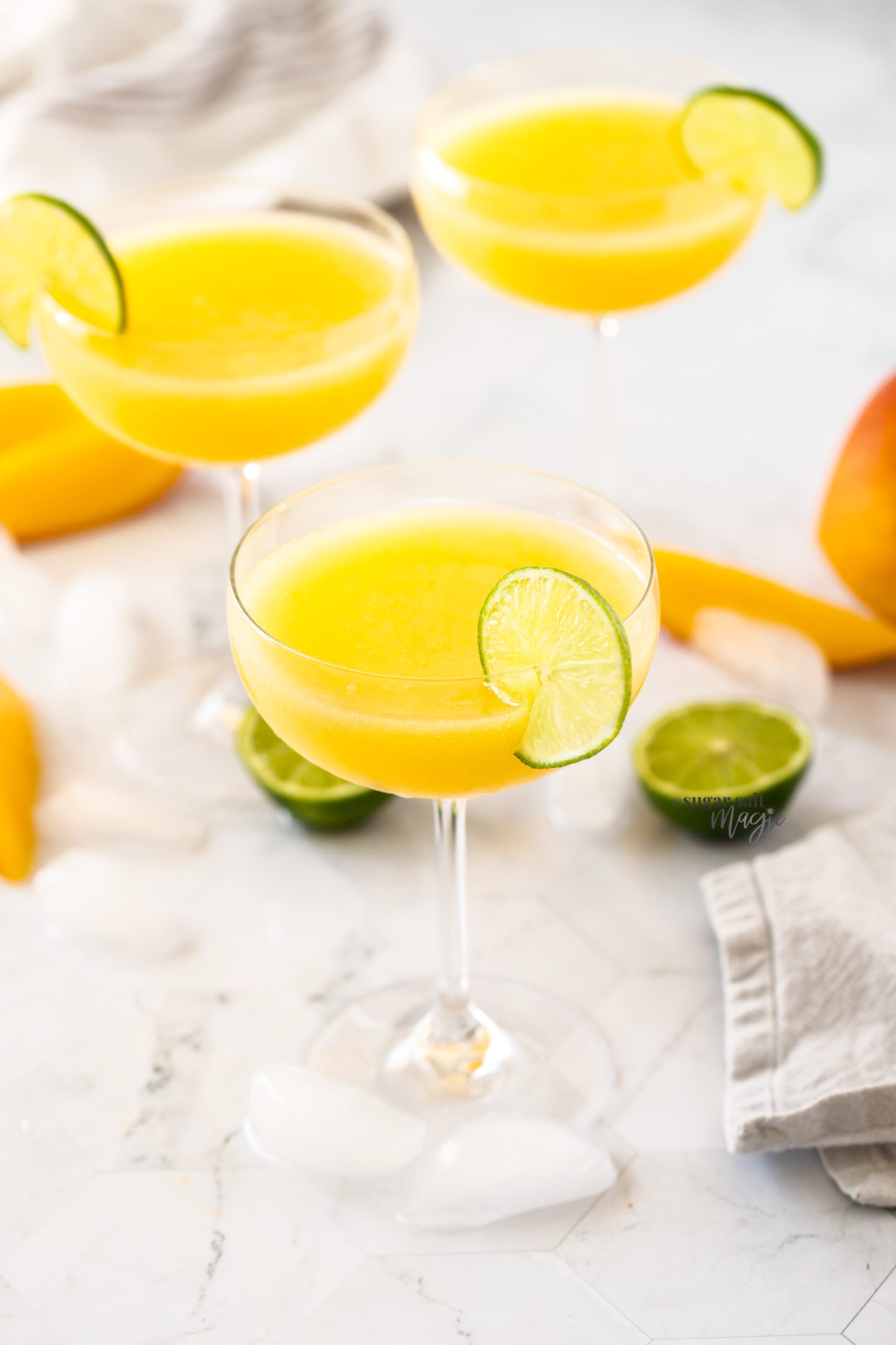 3 champagne saucers filled with mango daiquiri with a slice of lime on the edge