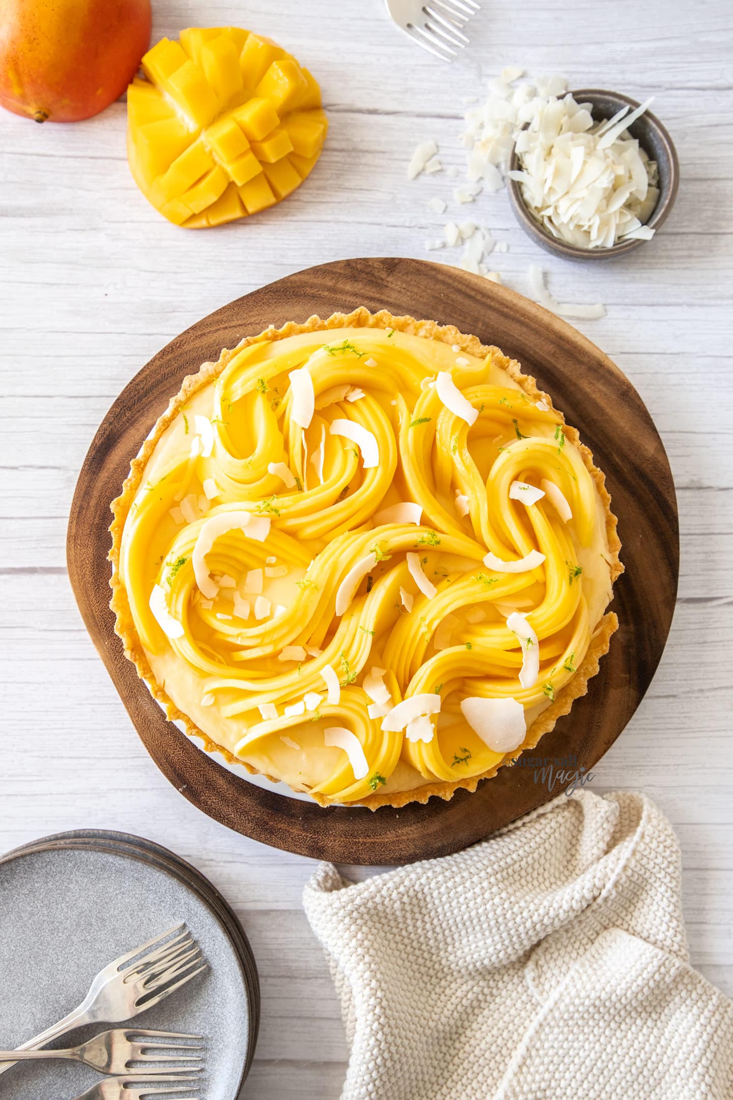 Top down view of a tart covered in sliced mango sitting on a wooden board.