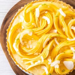 Top down view of a tart covered in sliced mango sitting on a wooden board