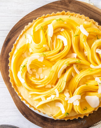 Top down view of a tart covered in sliced mango sitting on a wooden board