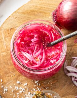 Bright pink onions in a glass jar on a wooden board.