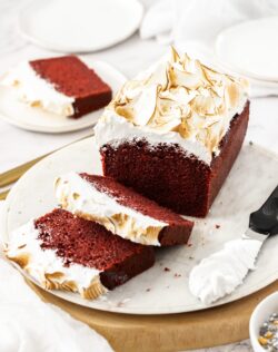Red velvet cake on a white platter with two slices cut from it.