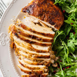 A golden turkey breast on a plate, partly sliced, with green salad on the side