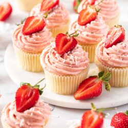 6 strawberry cupcakes on a white platter with a few more in front