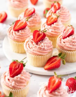6 strawberry cupcakes on a white platter with a few more in front