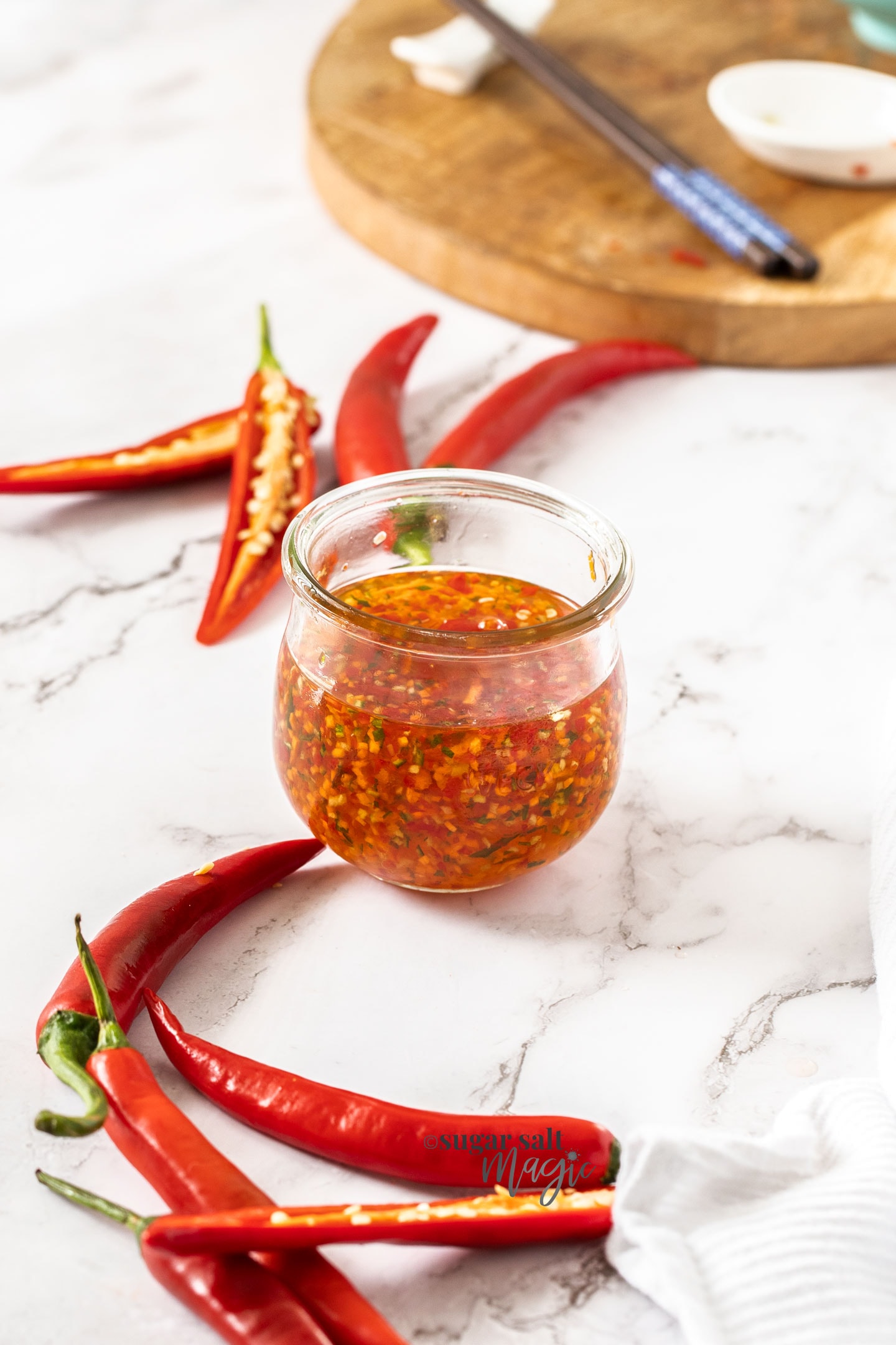 A glass jar filled with chilli sauce surrounded by chillis.